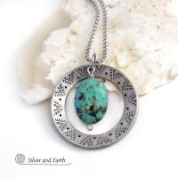 This handcrafted pendant necklace features a natural African turquoise gemstone dangling in front of a silver tone pewter circle with a hand stamped texture and oxidized finish. Unique and one of a kind, it has an earthy organic style with southwestern flair. Coordinating earrings sold separately.
