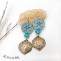 These handcrafted earrings feature gold brass dangles with a lightly hammered raw silk texture accented with glass flower beads and turquoise stone beads. The flower beads are a pretty shade of blue with golden highlights. They have an intricate carved and raised pattern on both sides of the beads. These earrings have a modern elegant, earthy chic style and will make a great gift for anyone that loves flowers and nature. They'll make a great addition to your spring / summer wardrobe - or any time of year.