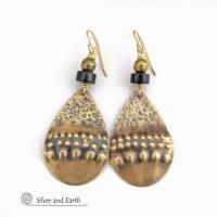 These handcrafted earrings feature gold brass teardrop dangles with a rustic hammered and hand stamped texture accented with matte black jasper stones and brass beads. They have an exotic, bohemian tribal vibe that makes a bold statement. Perfect for women that love to wear unique artisan handcrafted jewelry. Handmade in the USA by Silver and Earth Jewelry. 