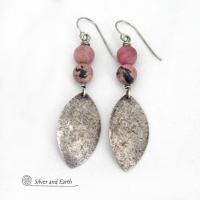 These sterling silver dangle earrings have a rustic lightly hammered texture and are accented with a stack of pink rhodonite gemstones. The stones have a pretty pink hue with a natural black spot matrix. They have a modern, contemporary style that coordinates well with all wardrobe types. 