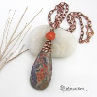 This handcrafted pendant necklace features a natural rhyolite jasper stone wire wrapped in copper wire and accented with a nugget-shaped coral bead. It has a natural pattern in several shades of earthy green along with splashes of orange. It has an earthy, casual boho style and is perfect for anyone that loves natural stones. It comes on an 18” copper chain with sturdy hook & eye closure; which can be removed from the pendant and worn alone or with other pendants in your wardrobe.