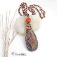 This handcrafted pendant necklace features a natural rhyolite jasper stone wire wrapped in copper wire and accented with a nugget-shaped coral bead. It has a natural pattern in several shades of earthy green along with splashes of orange. It has an earthy, casual boho style and is perfect for anyone that loves natural stones. It comes on an 18” copper chain with sturdy hook & eye closure; which can be removed from the pendant and worn alone or with other pendants in your wardrobe.