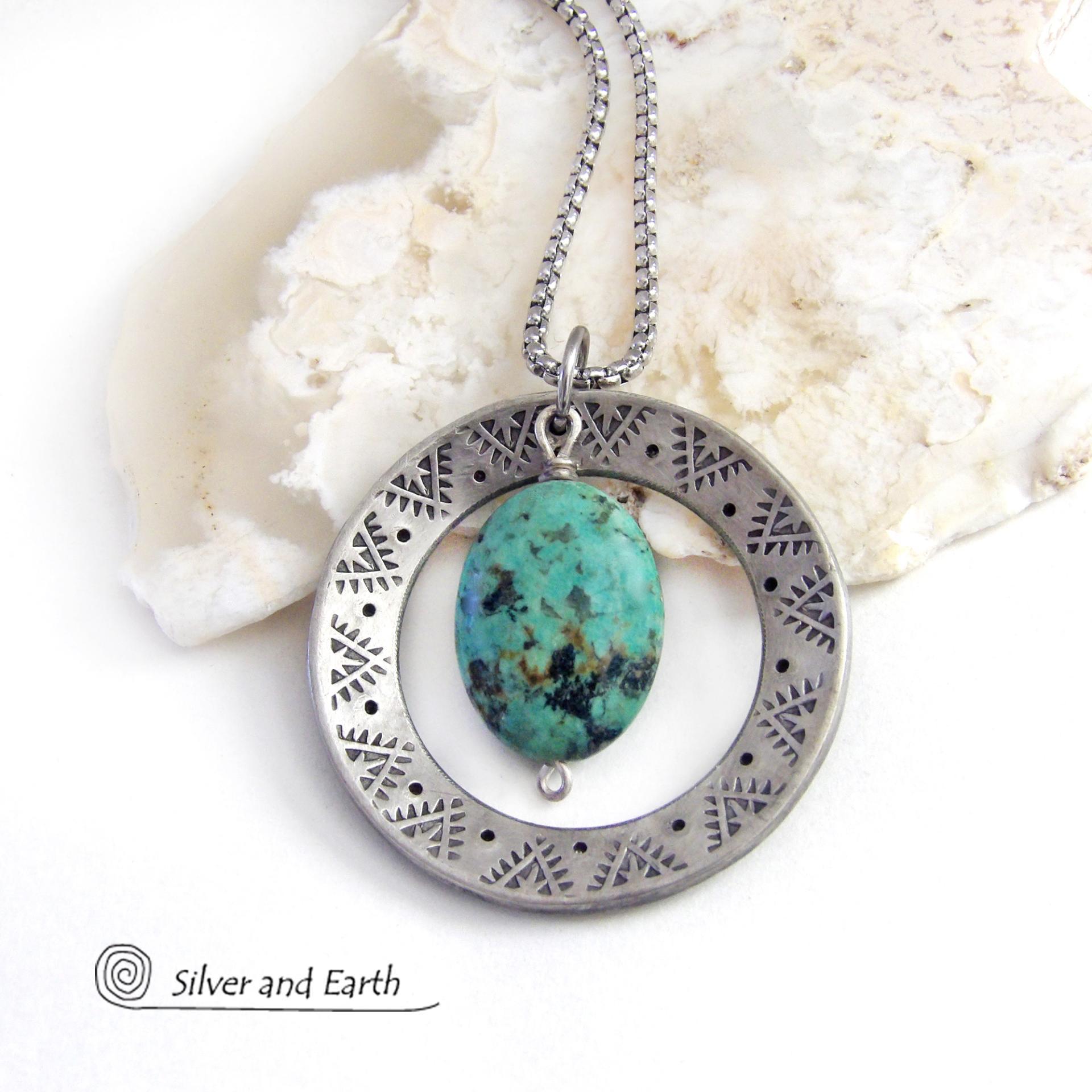 This handcrafted pendant necklace features a natural African turquoise gemstone dangling in front of a silver tone pewter circle with a hand stamped texture and oxidized finish. Unique and one of a kind, it has an earthy organic style with southwestern flair. Coordinating earrings sold separately.