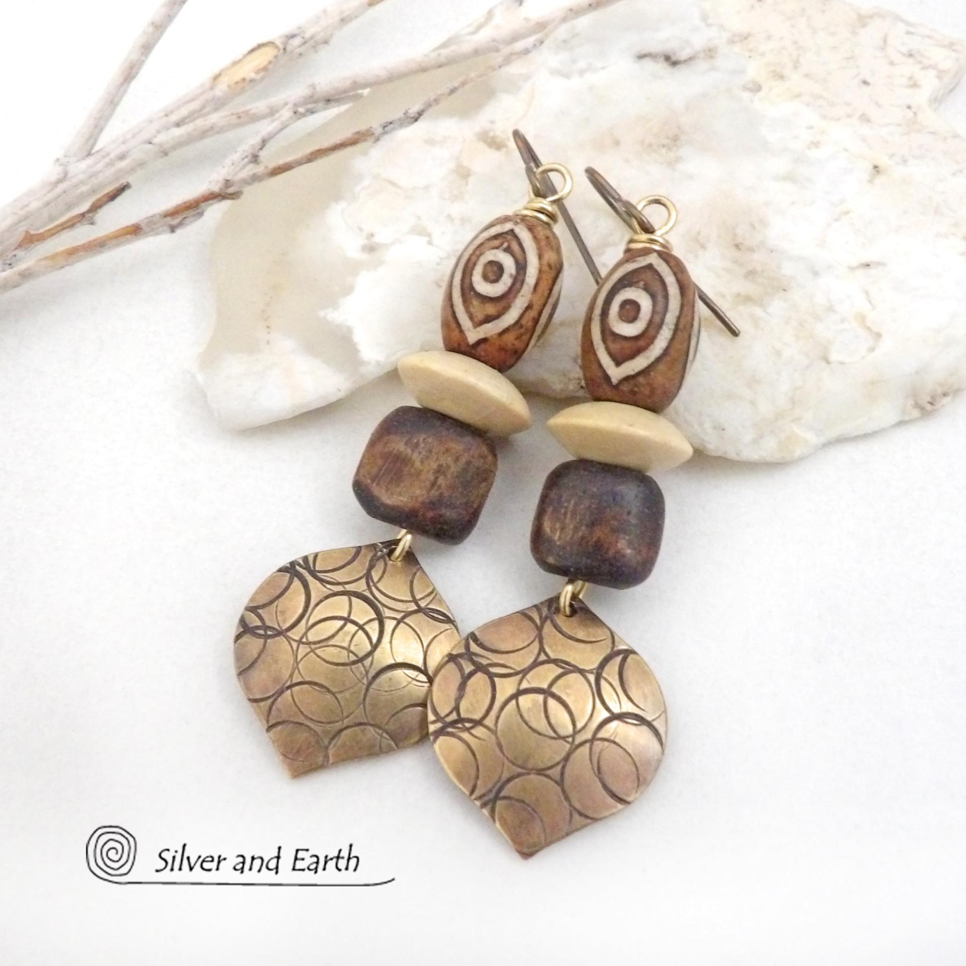 These handcrafted earrings feature gold brass dangles with a hand stamped texture accented with brown Tibetan etched agate stones, brown wood beads and tan wood saucer beads. Bold and unique, they have an ethnic tribal style with boho flair that makes a striking statement. Bold and striking, these handmade earrings are a beautiful example of bohemian-inspired jewelry.