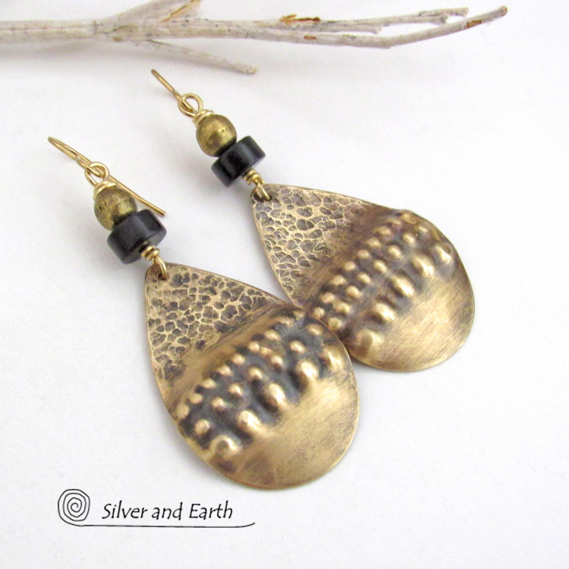 These handcrafted earrings feature gold brass teardrop dangles with a rustic hammered and hand stamped texture accented with matte black jasper stones and brass beads. They have an exotic, bohemian tribal vibe that makes a bold statement. Perfect for women that love to wear unique artisan handcrafted jewelry. Handmade in the USA by Silver and Earth Jewelry. 