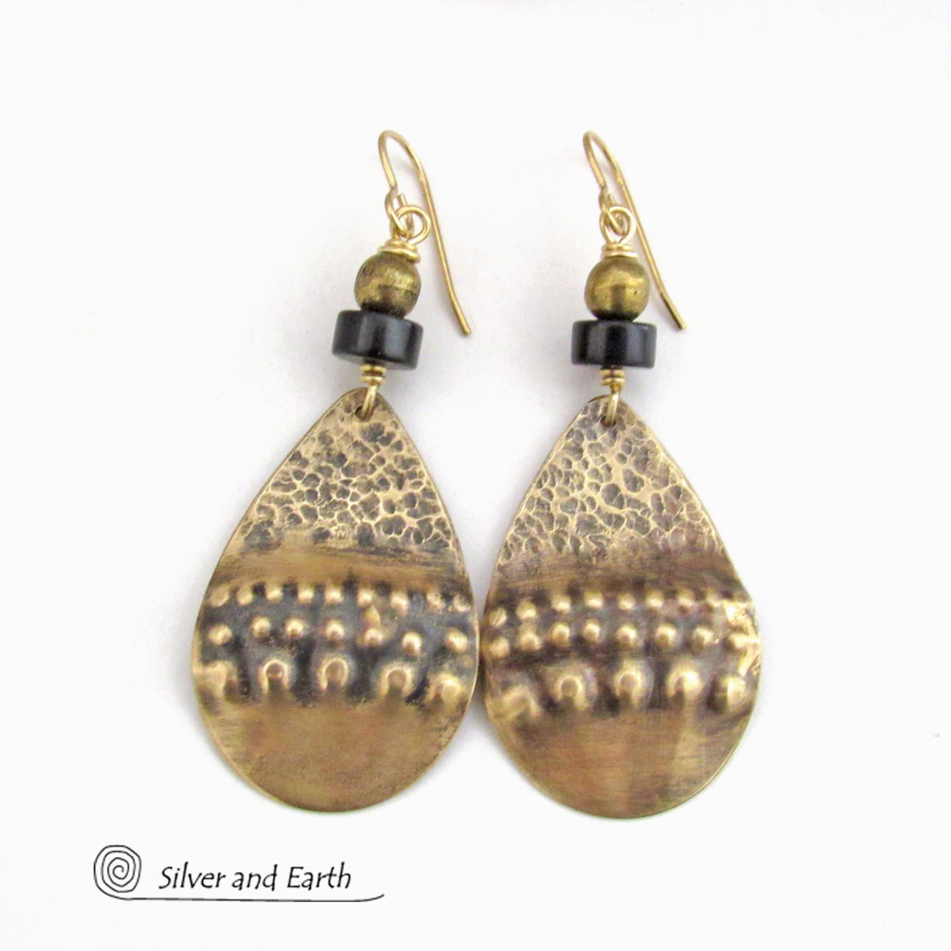 These handcrafted earrings feature gold brass teardrop dangles with a rustic hammered and hand stamped texture accented with matte black jasper stones and brass beads. They have an exotic, bohemian tribal vibe that makes a bold statement. Perfect for women that love to wear unique artisan handcrafted jewelry. Handmade in the USA by Silver and Earth Jewelry. 