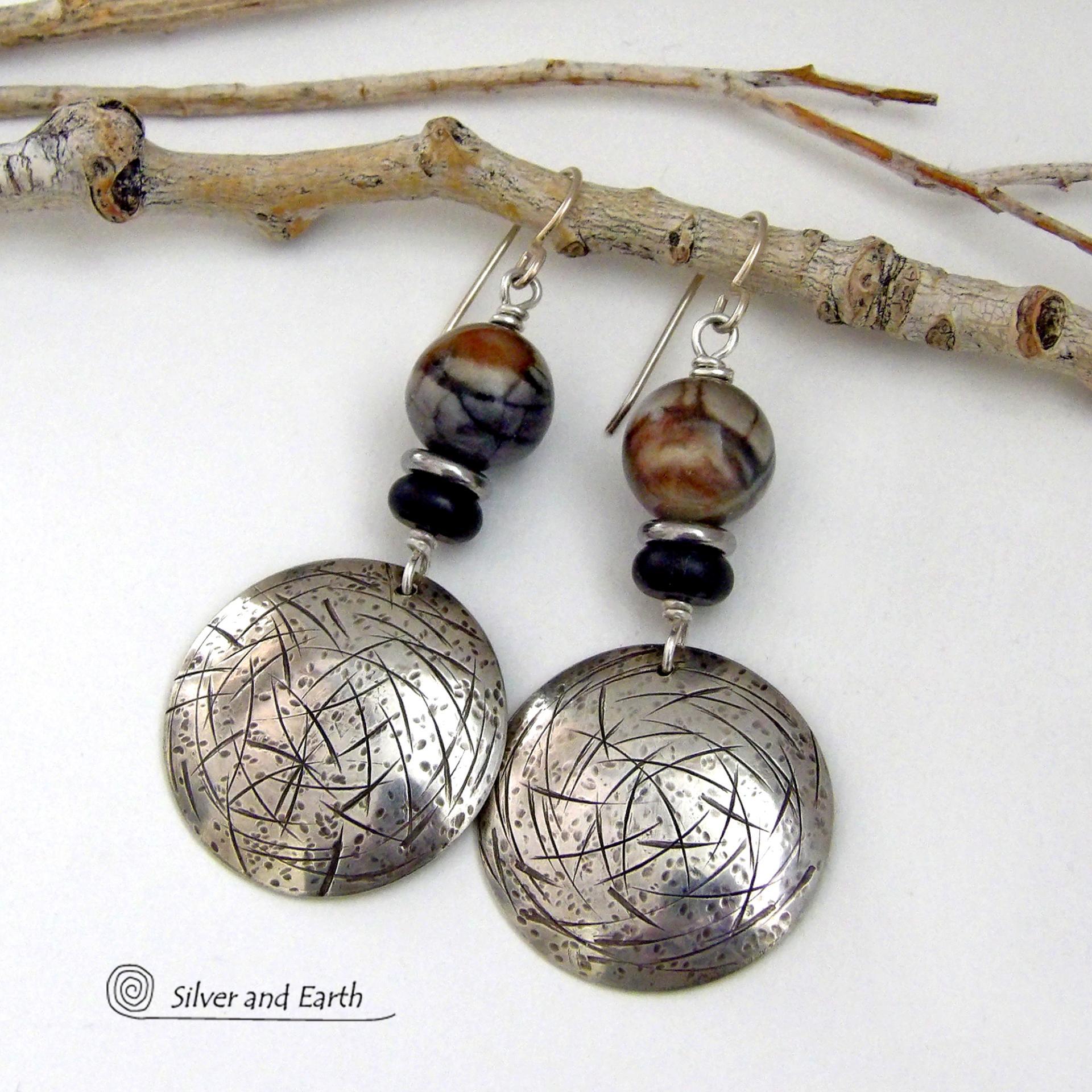These one-of-a-kind earrings feature handcrafted sterling silver with a hammered and hand stamped texture accented with earthy natural Picasso marble gemstones, black glass and stainless steel beads. This semiprecious stone is found only in southwest Utah. It's named after the famous artist because the natural matrix of geometric lines resembles an abstract painting. The stones in this pair have a beautiful matrix pattern of distinctive swirly lines in black, grey and chocolate brown.