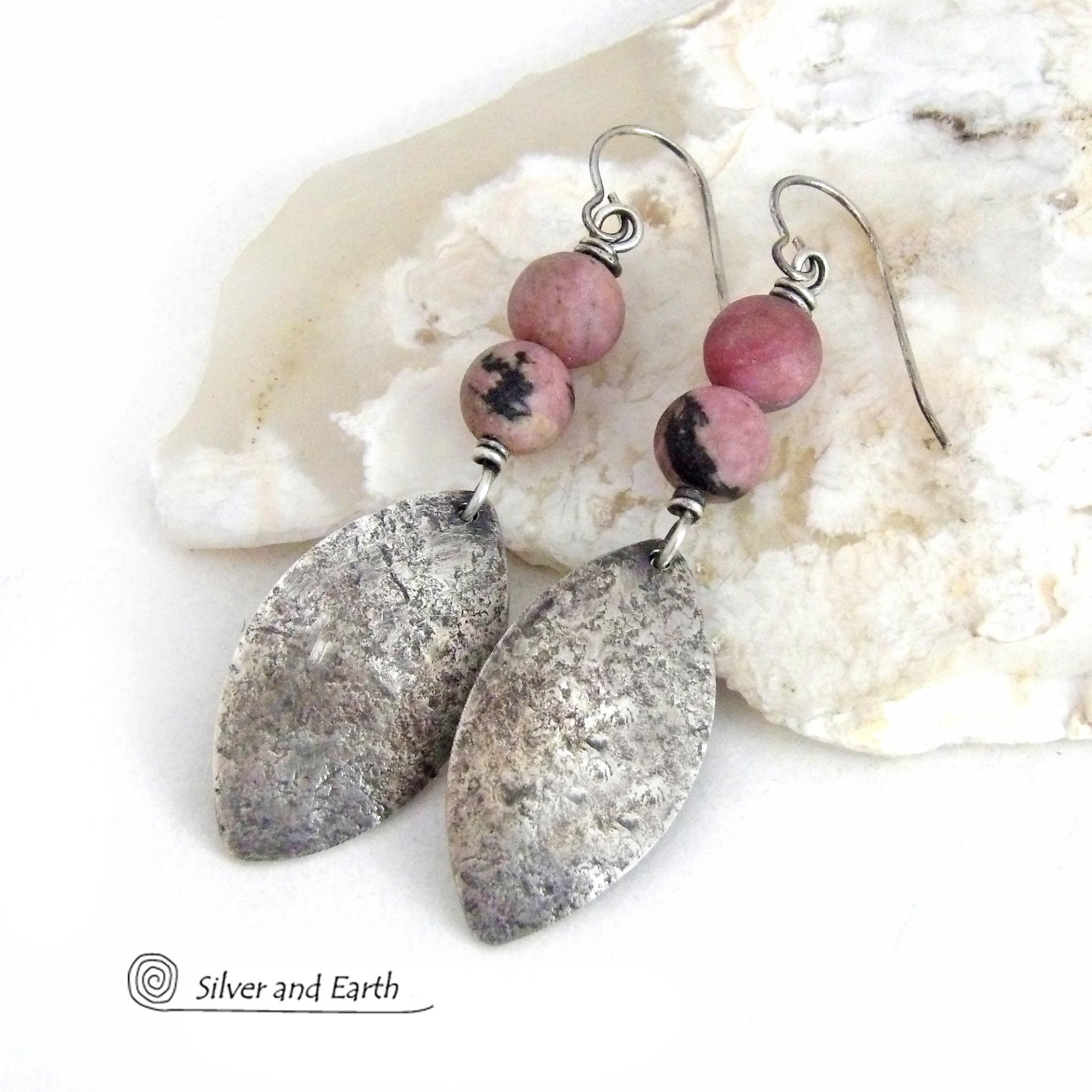 These sterling silver dangle earrings have a rustic lightly hammered texture and are accented with a stack of pink rhodonite gemstones. The stones have a pretty pink hue with a natural black spot matrix. They have a modern, contemporary style that coordinates well with all wardrobe types. 