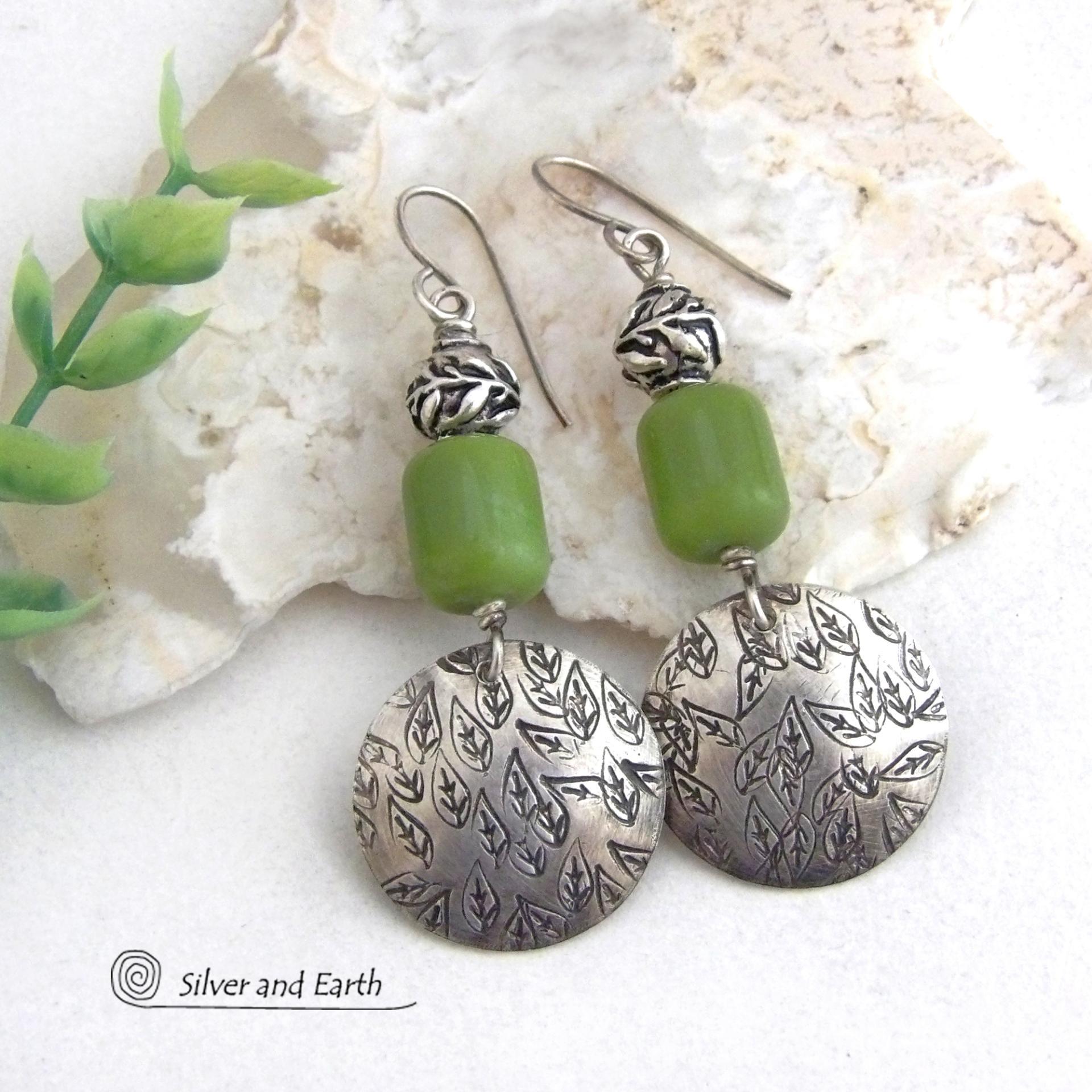 Sterling silver earrings with a hand stamped leaf design accented with natural green serpentine stones and silver pewter beads. The stones have a lime green hue and the pewter beads have a beautifully detailed 3-dimensional carved pattern of vines and leaves. They have a modern, earthy style and will make a great gift for a nature lover. The earrings are handmade and are a beautiful example of nature-inspired jewelry. 