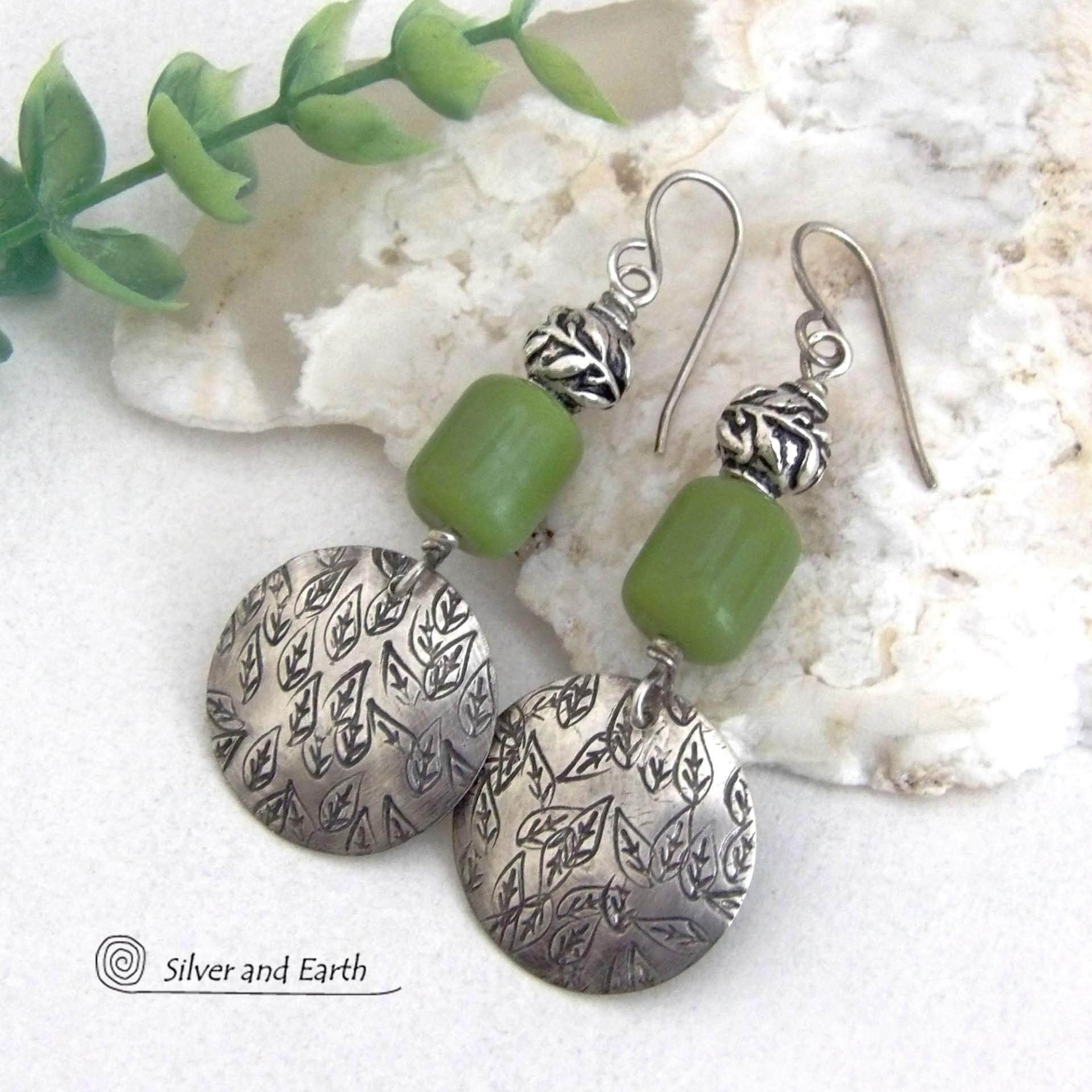 Sterling silver earrings with a hand stamped leaf design accented with natural green serpentine stones and silver pewter beads. The stones have a lime green hue and the pewter beads have a beautifully detailed 3-dimensional carved pattern of vines and leaves. They have a modern, earthy style and will make a great gift for a nature lover. The earrings are handmade and are a beautiful example of nature-inspired jewelry. 