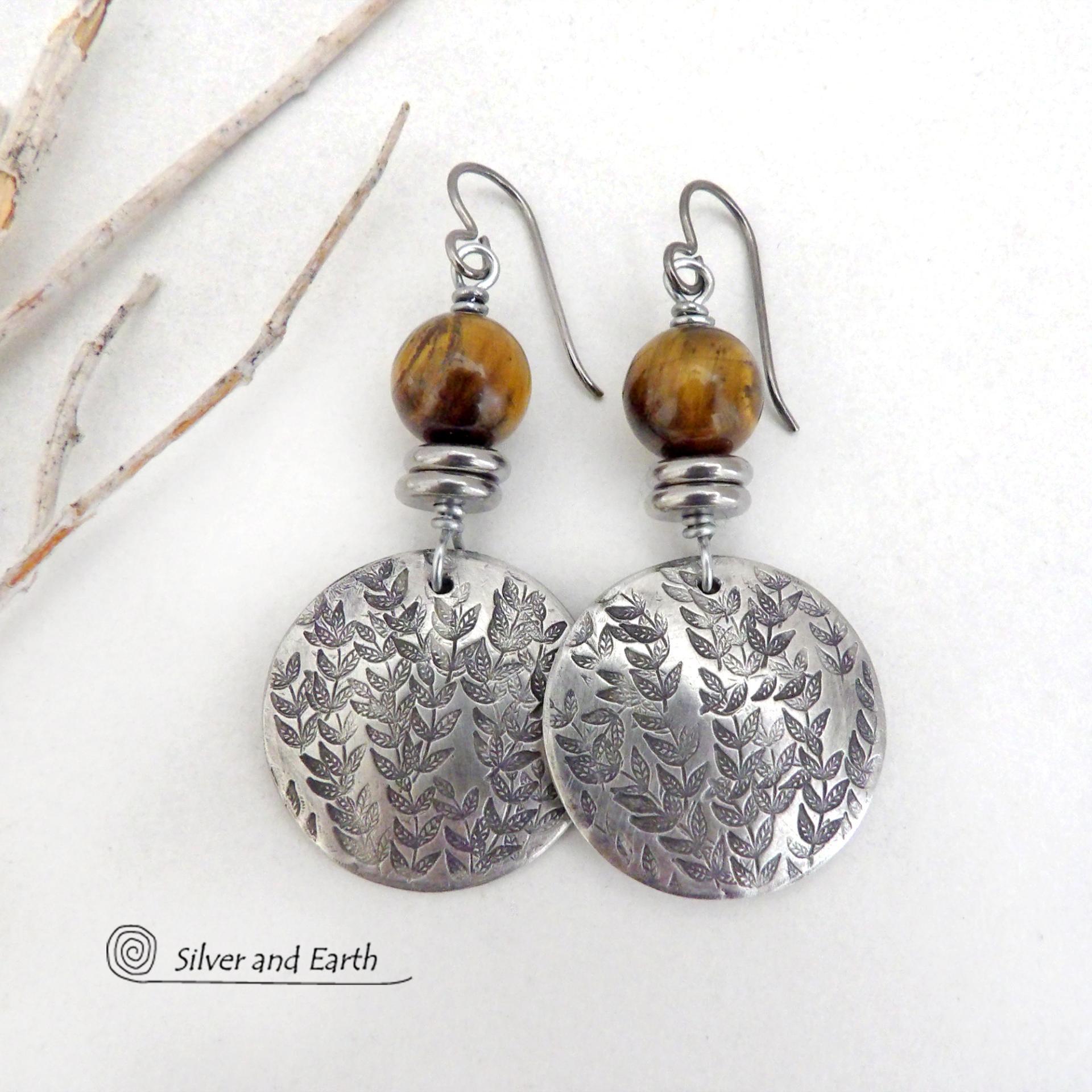 The earrings are handmade and are a beautiful example of nature-inspired jewelry. They feature solid pewter round discs with a hand stamped leaf design and are accented with brown tiger's eye gemstones and stainless steel beads.They showcase a beautiful hand stamped texture accented with high-quality natural gemstones and will make a great gift for a nature lover. Handmade by artist Silver and Earth, a New Mexico True Certified business. 