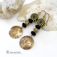These handcrafted earrings have an ethnic boho tribal vibe. They feature gold brass dangles with a hand stamped spiral and line texture accented with black and light yellow Fimo clay beads with a spiral design, black glass and brass beads. Unique and fun to wear - they have a funky bohemian vibe that makes a bold, striking statement. Perfect for women that love to wear one-of-a-kind artisan handcrafted jewelry. Handmade in the USA by Silver and Earth Jewelry. 