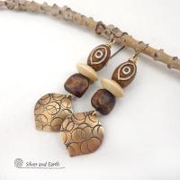 These handcrafted earrings feature gold brass dangles with a hand stamped texture accented with brown Tibetan etched agate stones, brown wood beads and tan wood saucer beads. Bold and unique, they have an ethnic tribal style with boho flair that makes a striking statement. Bold and striking, these handmade earrings are a beautiful example of bohemian-inspired jewelry.