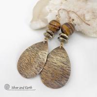 These handcrafted earrings feature textured gold brass teardrop dangles accented with natural brown tiger's eye gemstones and hematite stone beads. The beads have an electroplated champagne gold tone finish which adds a touch of shimmer and shine. They have an earthy modern style that coordinates well with all wardrobe styles. A matching necklace is availabe and sold separately. Handmade in the USA by Silver and Earth Jewelry.