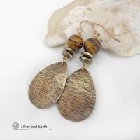 These handcrafted earrings feature textured gold brass teardrop dangles accented with natural brown tiger's eye gemstones and hematite stone beads. The beads have an electroplated champagne gold tone finish which adds a touch of shimmer and shine. They have an earthy modern style that coordinates well with all wardrobe styles. Handmade in the USA by Silver and Earth Jewelry.