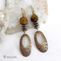 These handcrafted earrings feature gold brass oval hoop dangles with a hand stamped texture accented with natural brown tiger's eye gemstones and faceted hematite stones with an electroplated champagne gold finish. The stones have a beautiful brown hue with undertones of gold and a faceted finish which casts off a natural sparkle and shine. They have a modern, chic and elegant style that coordinates beautifully with all wardrobe types - dressed up or down.