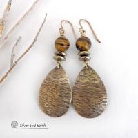 These handcrafted earrings feature textured gold brass teardrop dangles accented with natural brown tiger's eye gemstones and hematite stone beads. The beads have an electroplated champagne gold tone finish which adds a touch of shimmer and shine. They have an earthy modern style that coordinates well with all wardrobe styles. Handmade in the USA by Silver and Earth Jewelry.
