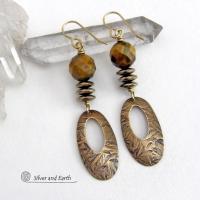 These handcrafted earrings feature gold brass oval hoop dangles with a hand stamped texture accented with natural brown tiger's eye gemstones and faceted hematite stones with an electroplated champagne gold finish. The stones have a beautiful brown hue with undertones of gold and a faceted finish which casts off a natural sparkle and shine. They have a modern, chic and elegant style that coordinates beautifully with all wardrobe types - dressed up or down.