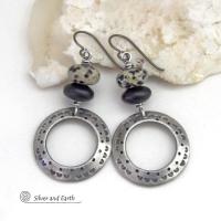 These handcrafted silver pewter hoop earrings have a hand stamped texture accented with natural dalmatian jasper gemstones and matte black glass beads. This type of jasper is known for its spotted pattern that resembles the Dalmatian breed of dog. These earrings have a modern, earthy boho chic style that coordinates beautifully with all wardrobe styles. Handmade the USA by Silver and Earth Jewelry.