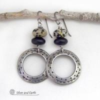 These handcrafted silver pewter hoop earrings have a hand stamped texture accented with natural dalmatian jasper gemstones and matte black glass beads. This type of jasper is known for its spotted pattern that resembles the Dalmatian breed of dog. These earrings have a modern, earthy boho chic style that coordinates beautifully with all wardrobe styles. Handmade the USA by Silver and Earth Jewelry.