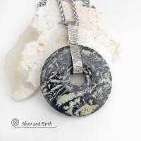 This one-of-a-kind pendant necklace features a stunning black fireworks jasper stone accented with a hand forged sterling silver bail. The stone has a natural dramatic pattern in hues of black with streaks of soft minty green and tan. The design is modern and bold - yet classic and always in fashion. It can be worn by either a man or a women. It's reversible and can be worn on either side. (See all photos for alternate sides).