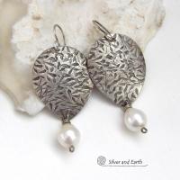 Perfect for everyday wear, these handcrafted sterling silver earrings are accented with dangling white freshwater pearls. The silver has an intricate hand stamped texture with an oxidized finish. The pearls contrast beautifully against the silver metal. They have an elegant, feminine feel with a contemporary design that looks great with all wardrobe styles. They'll make a great gift for someone born in June. Pearl is the traditional gemstone for this month. Handmade in the USA by Silver and Earth Jewelry. 