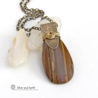 This handcrafted necklace features a natural brown tiger's eye gemstone accented with a gold brass bail. The stone has a beautiful matrix with earthy hues of brown and golden streaks. It has an earthy, modern style that coordinates beautifully with all wardrobe types. Unique and one of a kind, it makes a great gift for a natural stone lover - or a nice addition to your own jewelry collection.