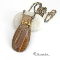 This handcrafted necklace features a natural brown tiger's eye gemstone accented with a gold brass bail. The stone has a beautiful matrix with earthy hues of brown and golden streaks. It has an earthy, modern style that coordinates beautifully with all wardrobe types. Unique and one of a kind, it makes a great gift for a natural stone lover - or a nice addition to your own jewelry collection.