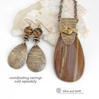 This handcrafted necklace features a natural brown tiger's eye gemstone accented with a gold brass bail. The stone has a beautiful matrix with earthy hues of brown and golden streaks. It has an earthy, modern style that coordinates beautifully with all wardrobe types. Unique and one of a kind, it makes a great gift for a natural stone lover - or a nice addition to your own jewelry collection. Matching earrings are available and sold separately. 