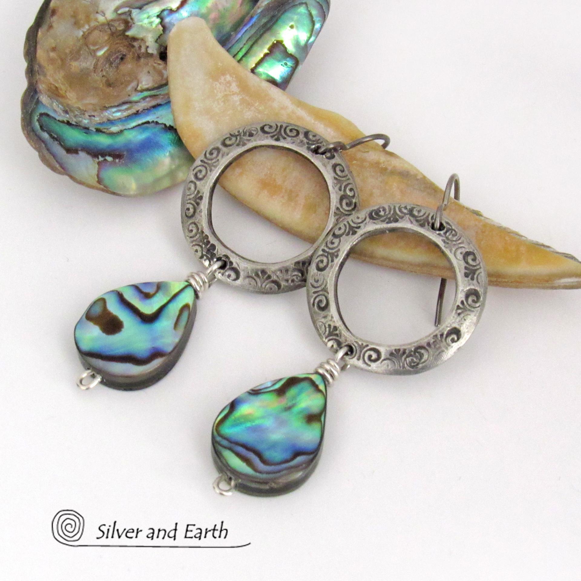 Vibrant natural abalone shells dangle from handcrafted silver pewter hoops in these modern stylish earrings. Each shell has its own unique pattern - with beautiful swirls and streaks of peacock blue, green, purple, silver and charcoal and a lovely iridescent shine. Lightweight and comfortable to wear, they'll look great with all wardrobe styles. 