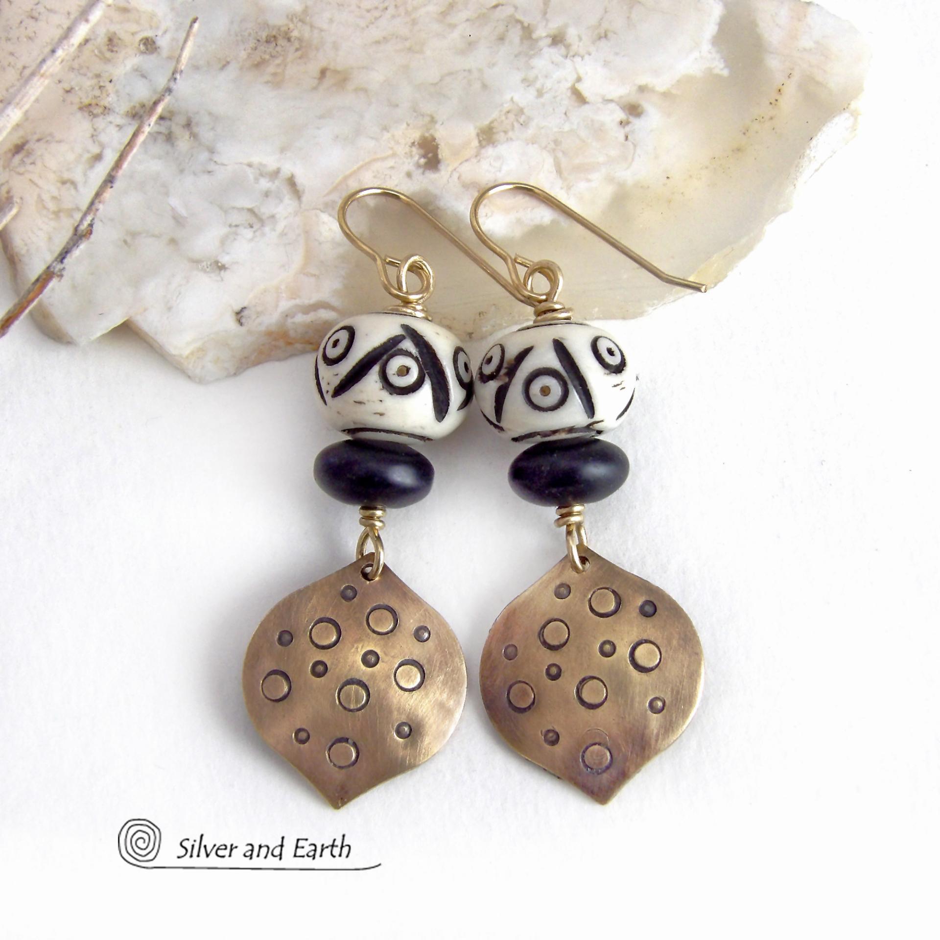 These handcrafted gold brass earrings have an ethnic, boho tribal vibe that makes a unique bold statement. They feature brass drops with a hand stamped texture accented with African carved bone beads with a bold pattern of dots and lines and matte black glass beads. Perfect for women that love unique handmade jewelry. Handmade in the USA by Silver and Earth Jewelry.