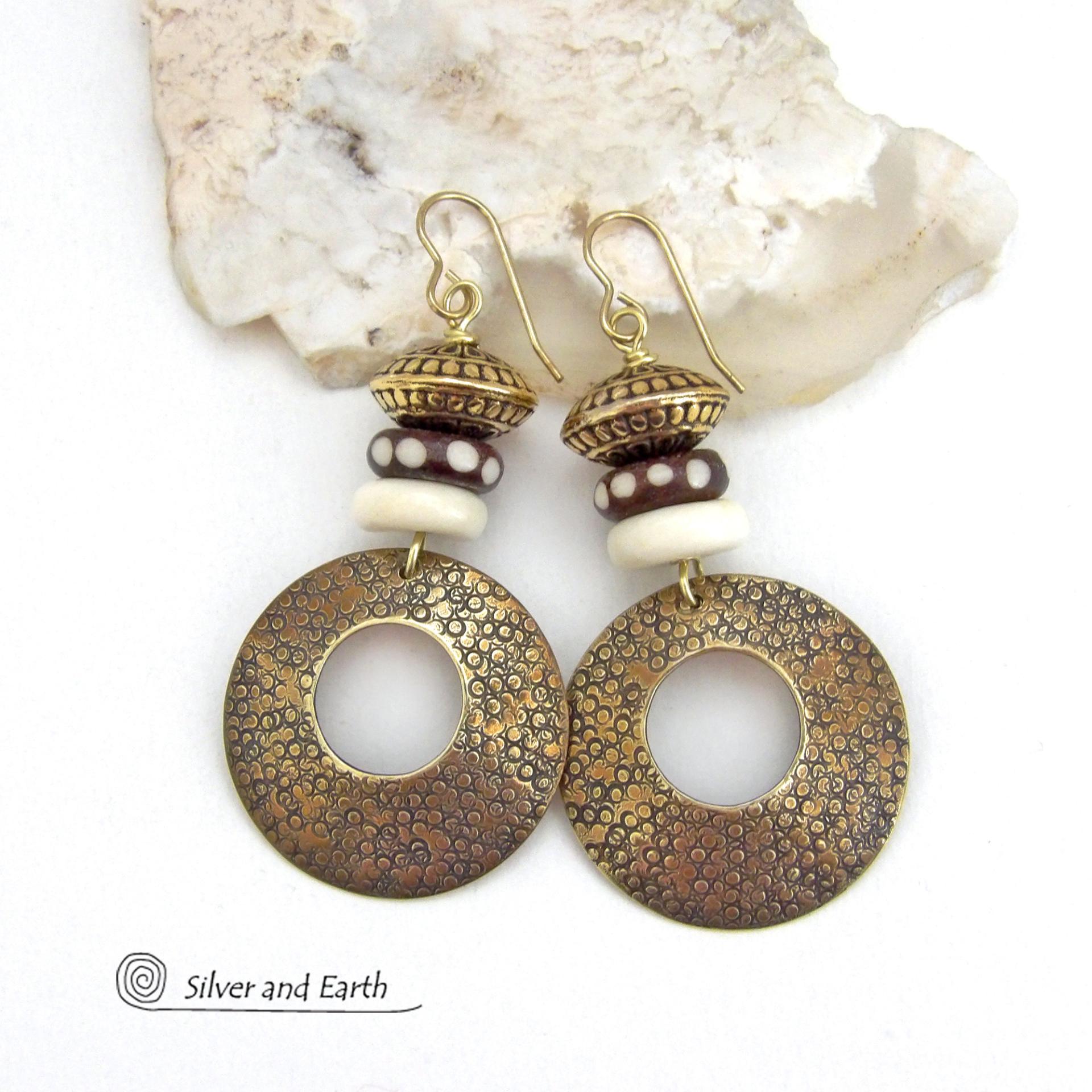 Big and bold, these handcrafted gold brass hoop earrings have a hand stamped texture and are accented with African batik bone dark brown beads with a dotted pattern, off-white bone beads and textured gold brass beads. They have an exotic ethnic and boho chic vibe that makes a striking, unique statement. Handmade in the USA by Silver and Earth Jewelry.