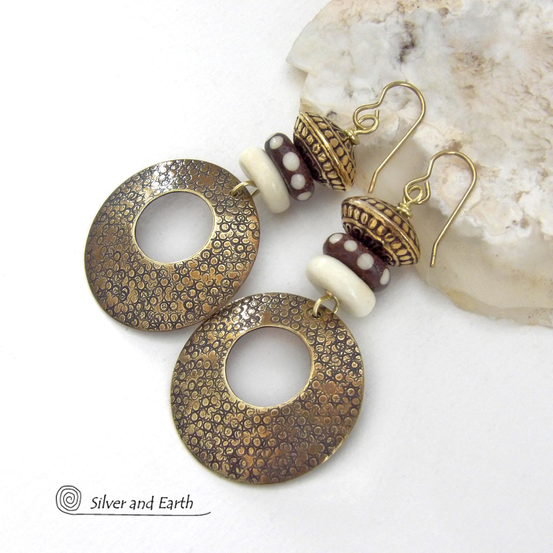 Big and bold, these handcrafted gold brass hoop earrings have a hand stamped texture and are accented with African batik bone dark brown beads with a dotted pattern, off-white bone beads and textured gold brass beads. They have an exotic ethnic and boho chic vibe that makes a striking, unique statement. Handmade in the USA by Silver and Earth Jewelry.