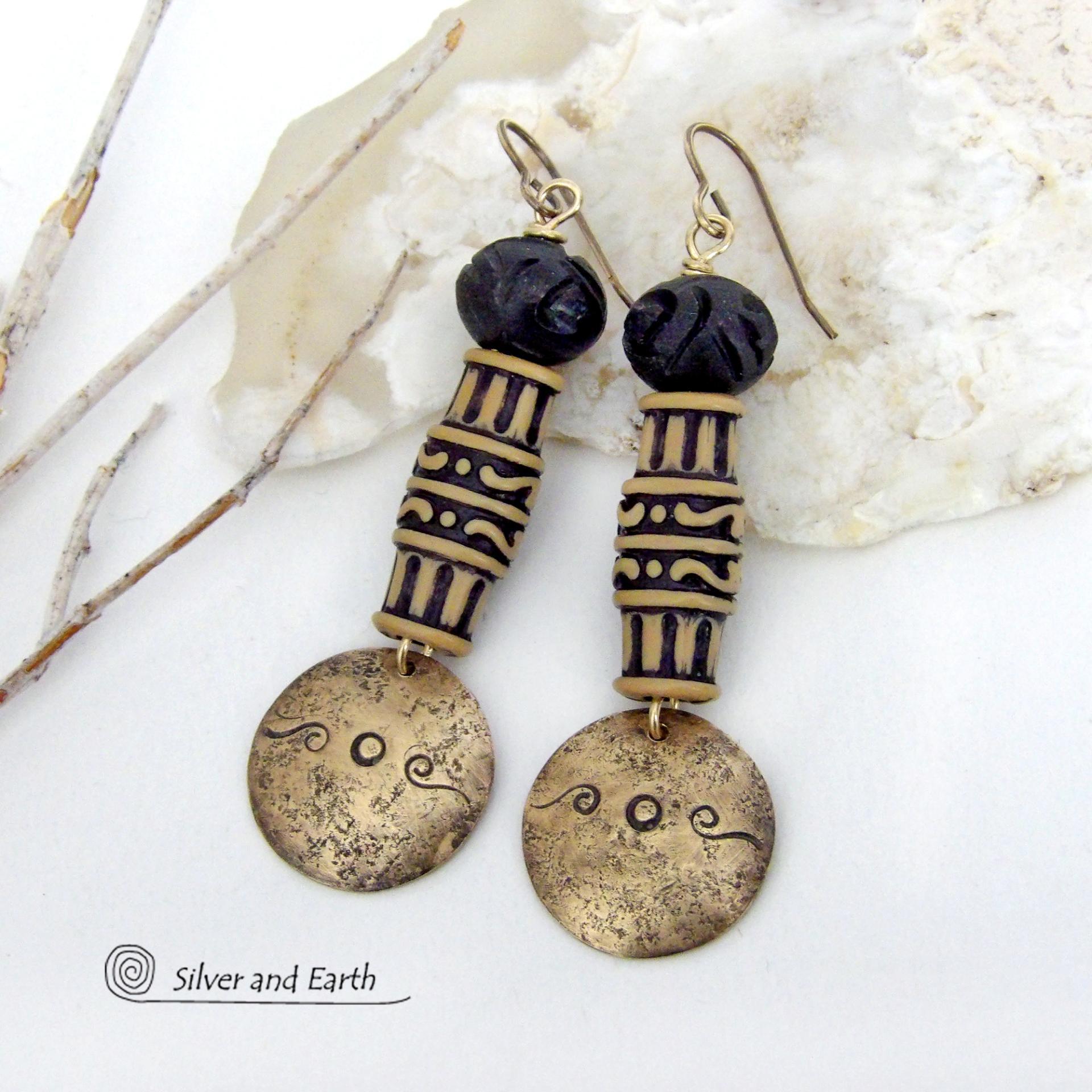 Bold and unique, these handcrafted earrings have an ethnic African tribal vibe. They feature gold brass dangles with a hand stamped and lightly hammered background texture accented with African beads with an intricately carved brownish-black and tan pattern topped off with black African carved bone beads. Unique and fun to wear - they'll make a bold, striking statement. Perfect for women that love to wear one-of-a-kind artisan handcrafted jewelry. Handmade in the USA by Silver and Earth Jewelry.