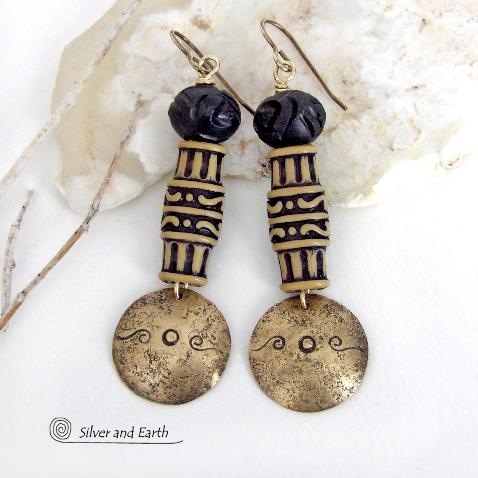 Bold and unique, these handcrafted earrings have an ethnic African tribal vibe. They feature gold brass dangles with a hand stamped and lightly hammered background texture accented with African beads with an intricately carved brownish-black and tan pattern topped off with black African carved bone beads. Unique and fun to wear - they'll make a bold, striking statement. Perfect for women that love to wear one-of-a-kind artisan handcrafted jewelry. Handmade in the USA by Silver and Earth Jewelry.