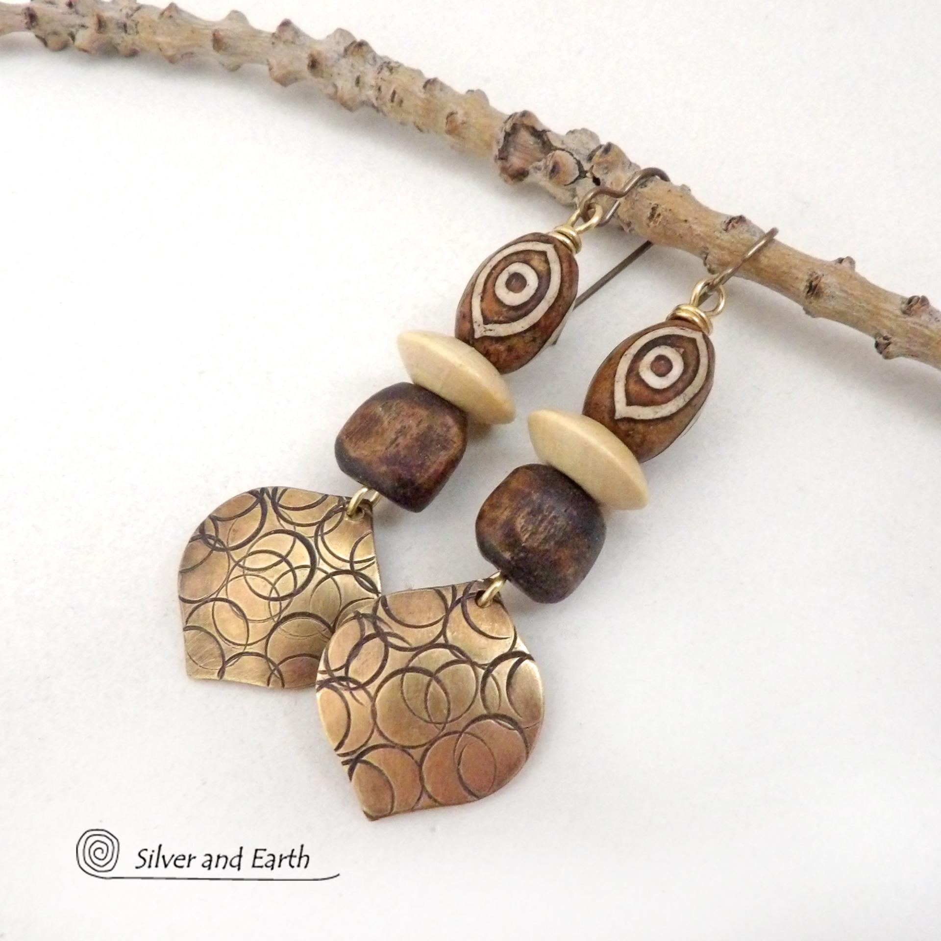 These handcrafted earrings feature gold brass dangles with a hand stamped texture accented with brown Tibetan etched agate stones, brown wood beads and tan wood saucer beads. Bold and unique, they have an ethnic tribal style with boho flair that makes a striking statement. Bold and striking, these handmade earrings are a beautiful example of bohemian-inspired jewelry.