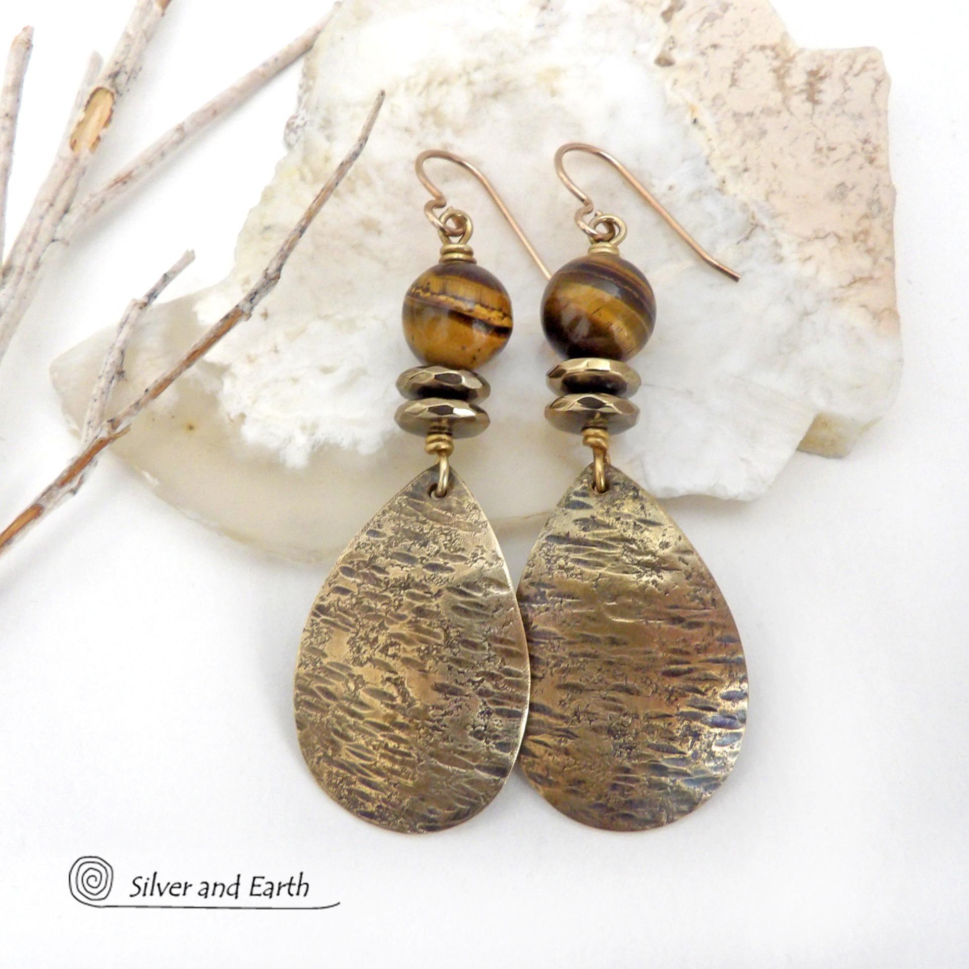 These handcrafted earrings feature textured gold brass teardrop dangles accented with natural brown tiger's eye gemstones and hematite stone beads. The beads have an electroplated champagne gold tone finish which adds a touch of shimmer and shine. They have an earthy modern style that coordinates well with all wardrobe styles. Handmade in the USA by Silver and Earth Jewelry.