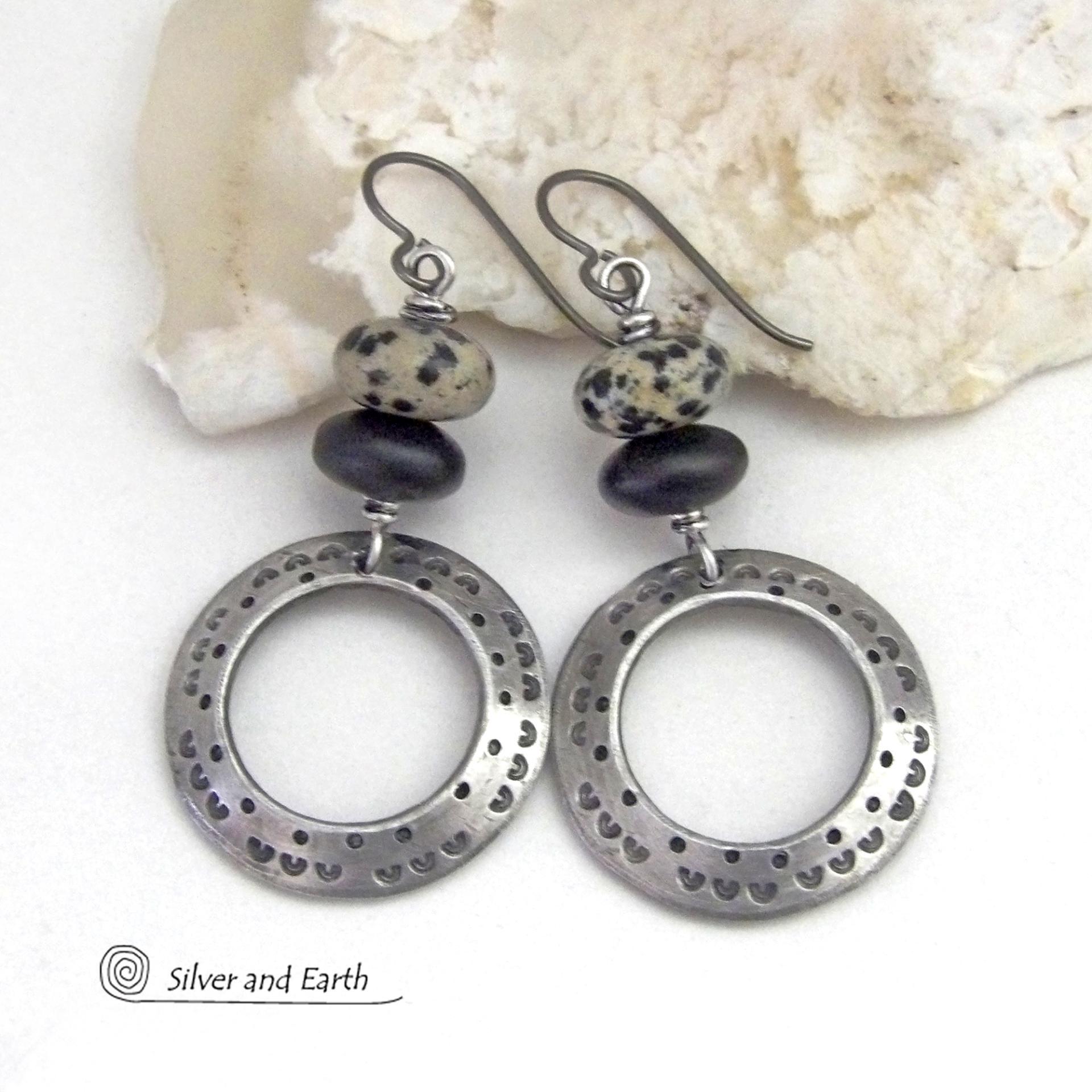 These handcrafted silver pewter hoop earrings have a hand stamped texture accented with natural dalmatian jasper gemstones and matte black glass beads. This type of jasper is known for its spotted pattern that resembles the Dalmatian breed of dog. These earrings have a modern, earthy boho chic style that coordinates beautifully with all wardrobe styles. Handmade the USA by Silver and Earth Jewelry.