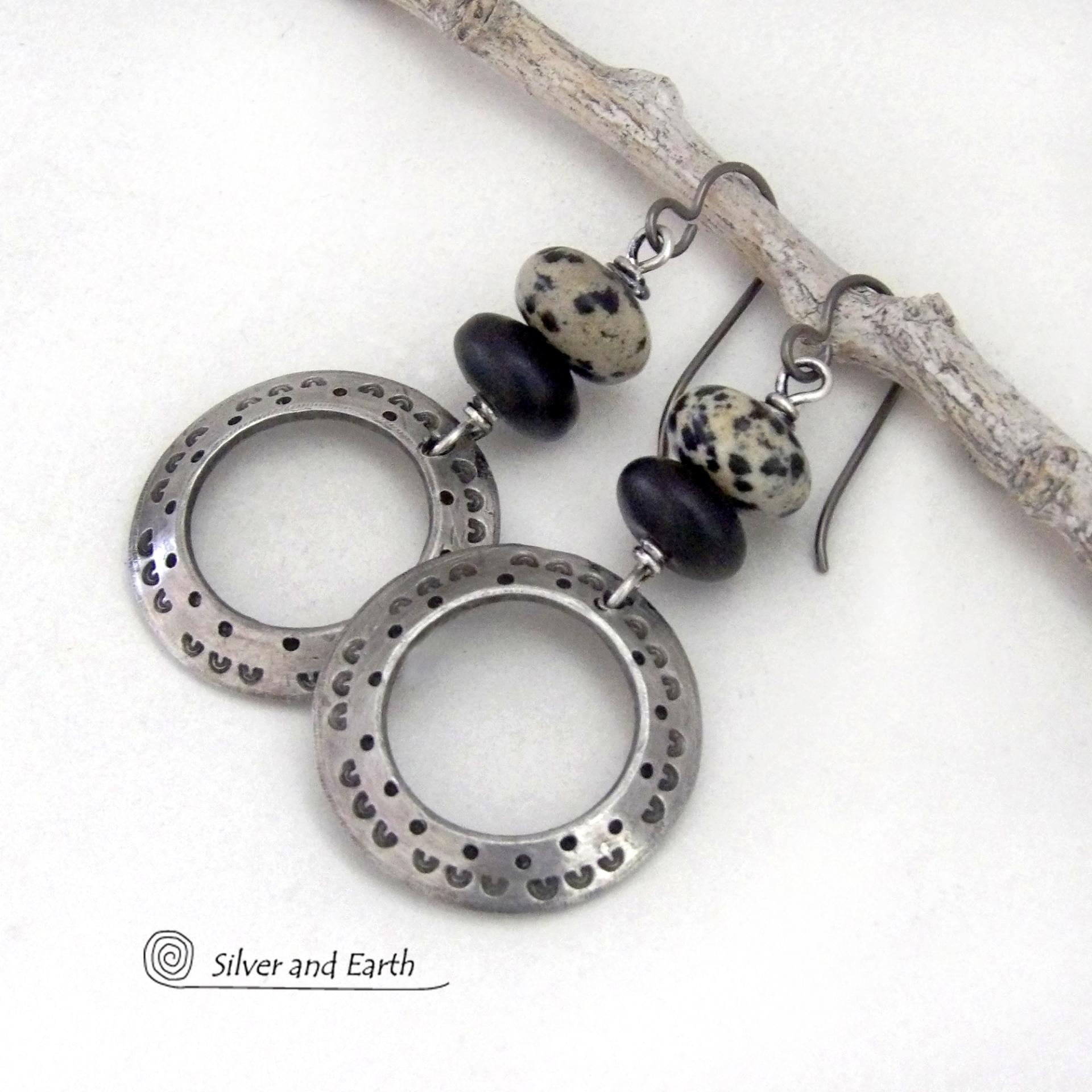 These handcrafted silver pewter hoop earrings have a hand stamped texture accented with natural dalmatian jasper gemstones and matte black glass beads. This type of jasper is known for its spotted pattern that resembles the Dalmatian breed of dog. These earrings have a modern, earthy boho chic style that coordinates beautifully with all wardrobe styles. Handmade the USA by Silver and Earth Jewelry.