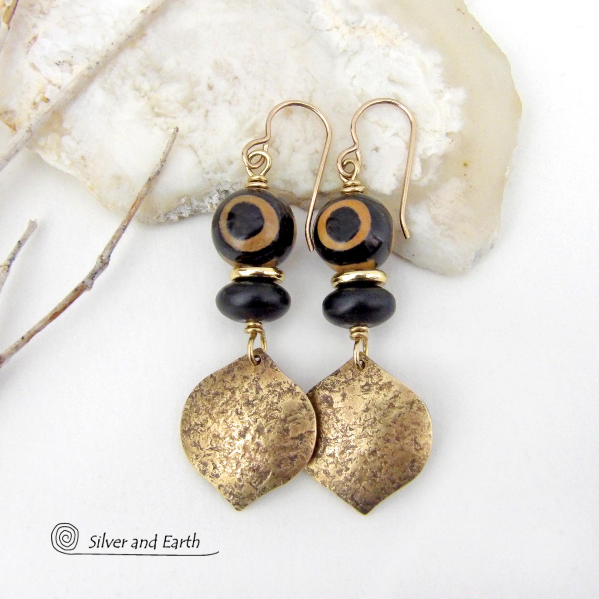 These handcrafted gold brass earrings have a contemporary modern style with an ethnic boho vibe. They feature brass drops with a lightly hammered texture accented with Tibetan eye agate gemstones, black glass and shiny brass beads. Bold and unique, they'll make a striking statement. Handmade in the USA by Silver and Earth Jewelry. 