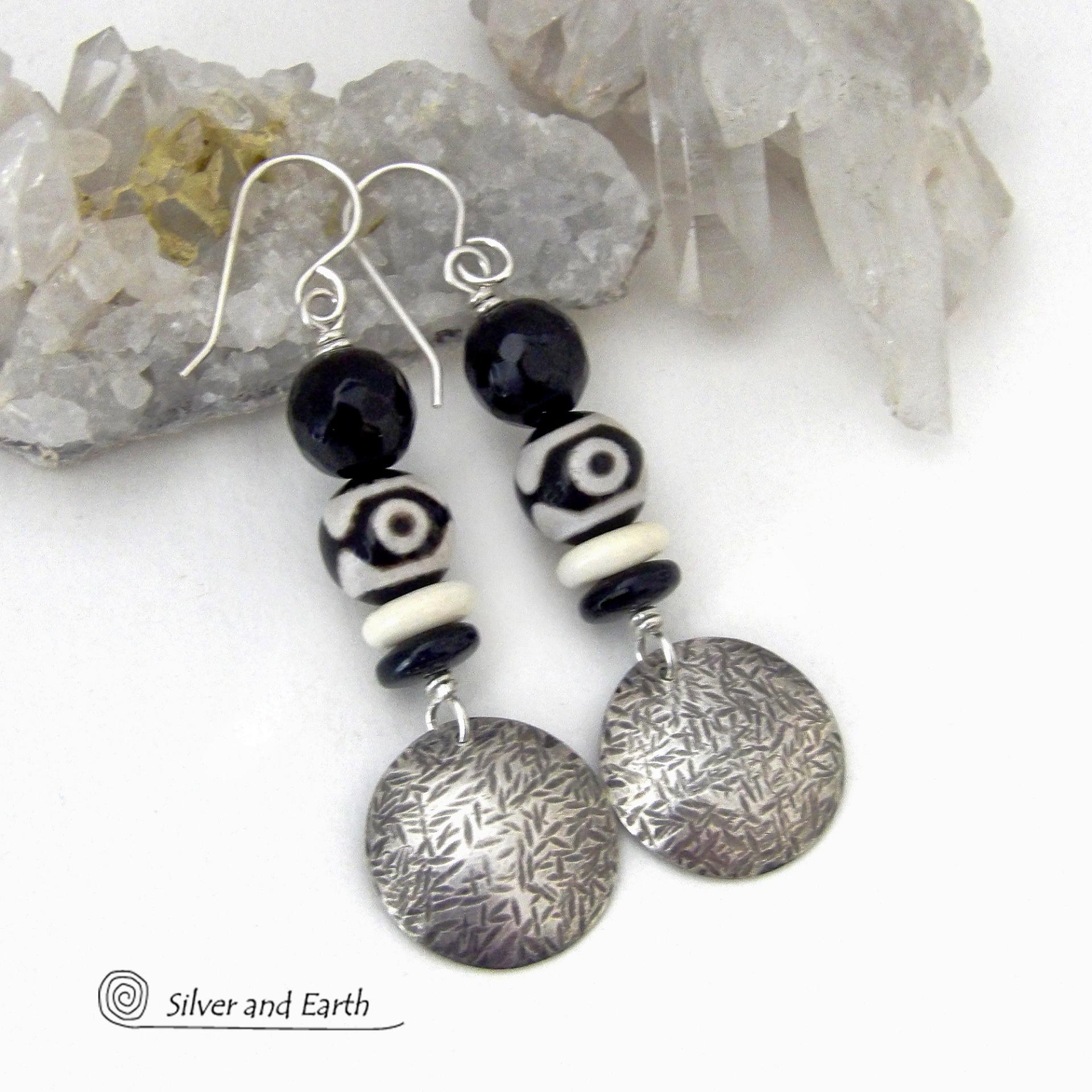 These earrings have a modern style with an ethnic tribal vibe. They feature handcrafted sterling silver circle dangles with a hammered texture accented with black and white Tibetan eye agate gemstones, onyx and bone beads, topped off with round black onyx gemstones with a faceted finish. Unique and striking, they'll make a bold statement. 