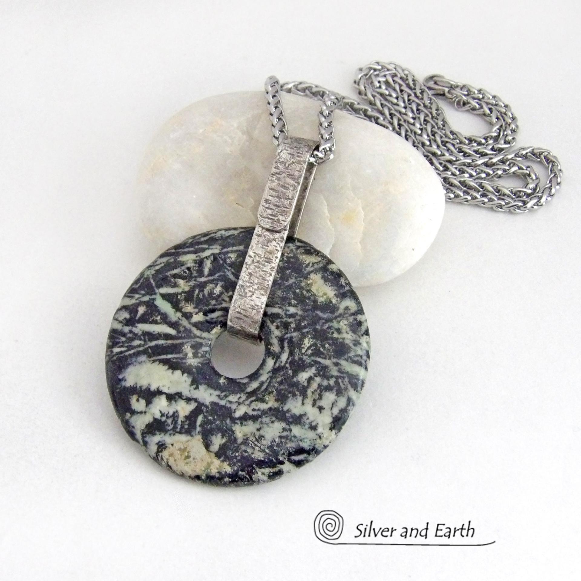 This one-of-a-kind pendant necklace features a stunning black fireworks jasper stone accented with a hand forged sterling silver bail. The stone has a natural dramatic pattern in hues of black with streaks of soft minty green and tan. The design is modern and bold - yet classic and always in fashion. It can be worn by either a man or a women. It's reversible and can be worn on either side. (See all photos for alternate sides).