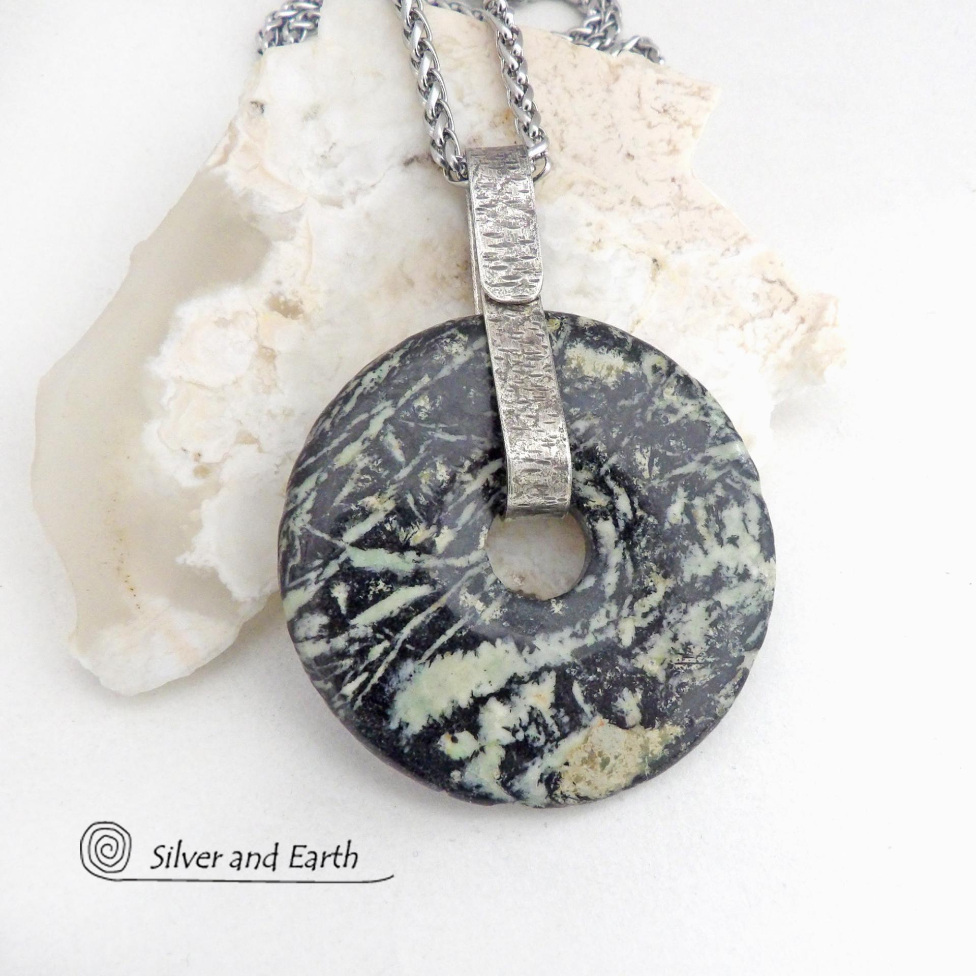 This one-of-a-kind pendant necklace features a stunning black fireworks jasper stone accented with a hand forged sterling silver bail. The stone has a natural dramatic pattern in hues of black with streaks of soft minty green and tan. The design is modern and bold - yet classic and always in fashion. It can be worn by either a man or a women. It's reversible and can be worn on either side. (See all photos for alternate sides).