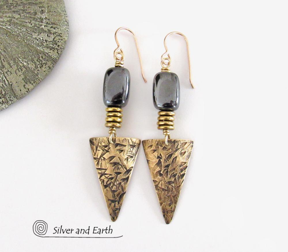 These gold brass triangle earrings have a hand stamped texture and are accented with natural hematite nugget-shaped gemstones on top of a stack of tiny brass beads. They have a modern contemporary and edgy style that makes a bold statement.