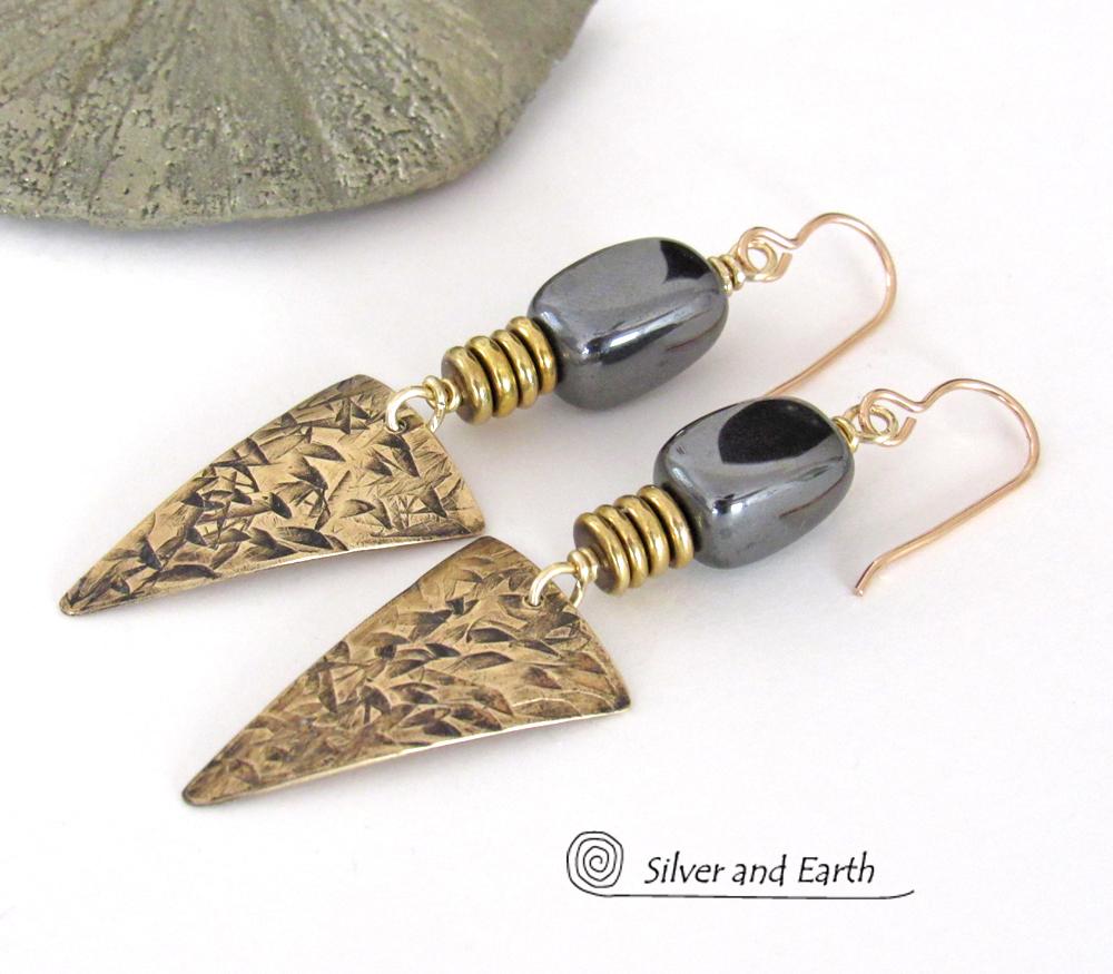 These gold brass triangle earrings have a hand stamped texture and are accented with natural hematite nugget-shaped gemstones on top of a stack of tiny brass beads. They have a modern contemporary and edgy style that makes a bold statement.