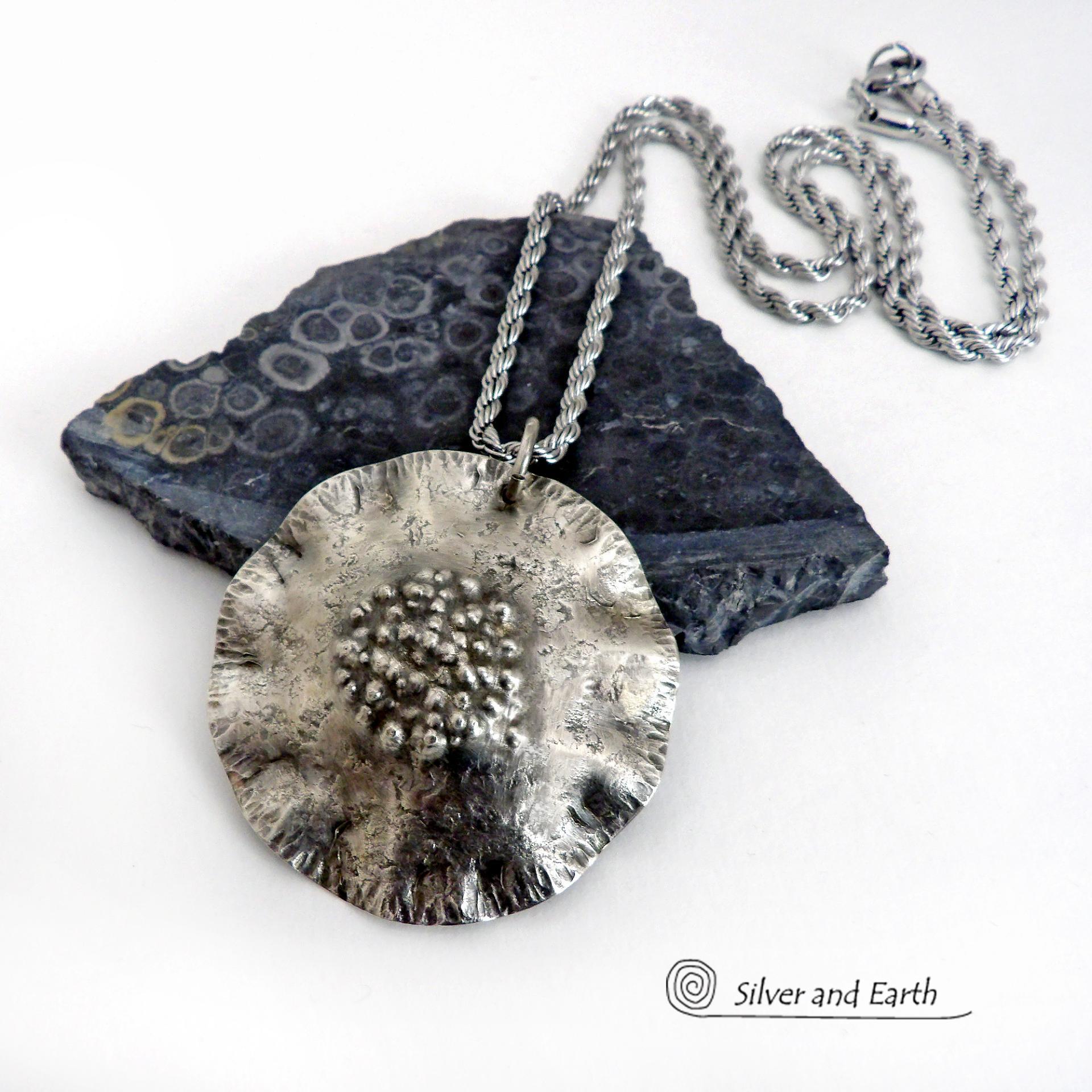 This handcrafted sterling silver necklace has a modern, earthy organic vibe. Perfect for everyday wear - it goes with everything. It features a large sterling silver circle with a rustic, hand forged texture and crimped ruffled edges.  Big and bold, it's sure to make an eye-catching statement. Handmade in the USA by Silver and Earth, a New Mexico True Certified business.  