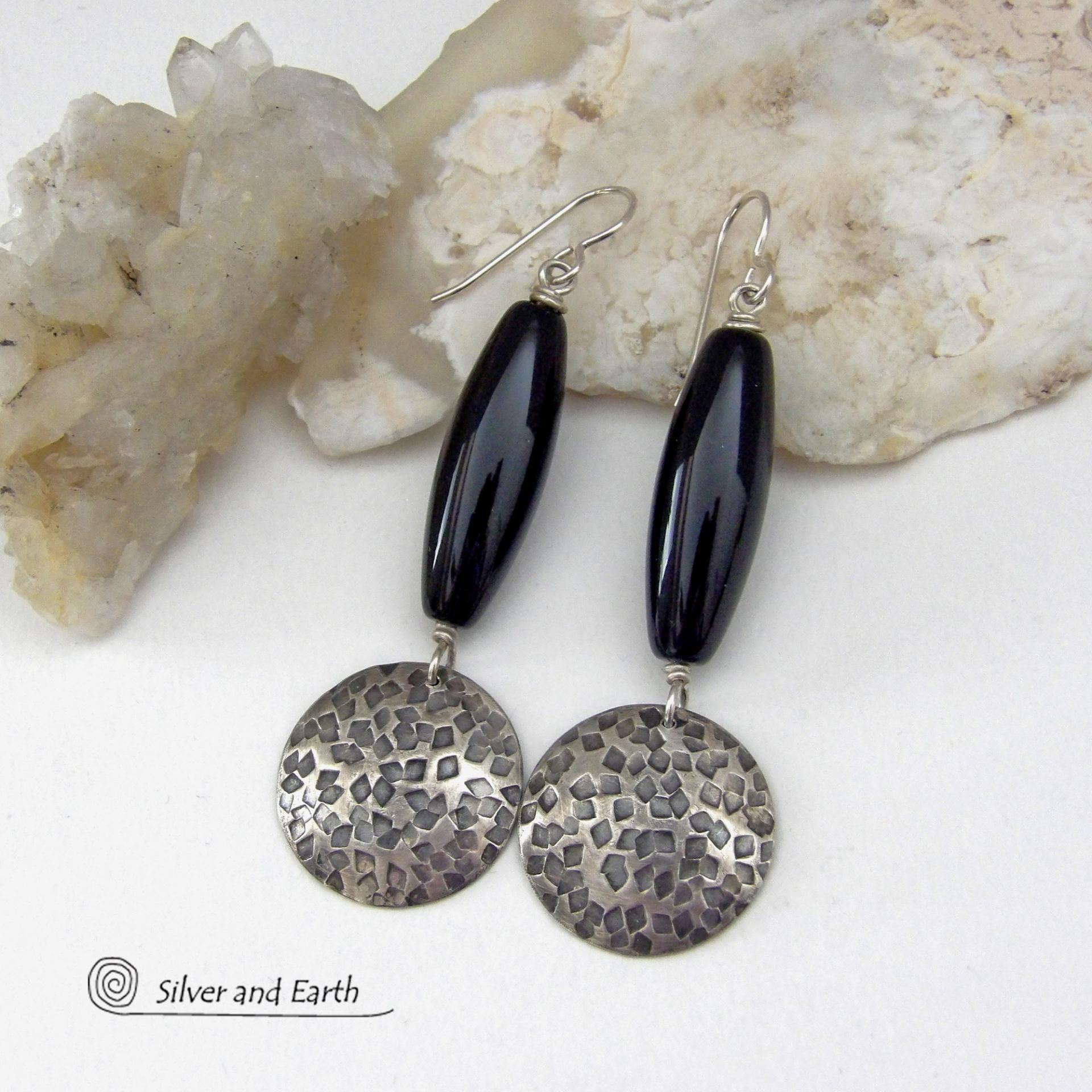 These handcrafted sterling silver dangle earrings have a hand stamped texture and oxidized finish and feature long black onyx gemstones. The stones are cut into a unique, elongated tubular shape and have a rich black hue and high polish. They have a modern, contemporary style that will look great with all wardrobe types. 