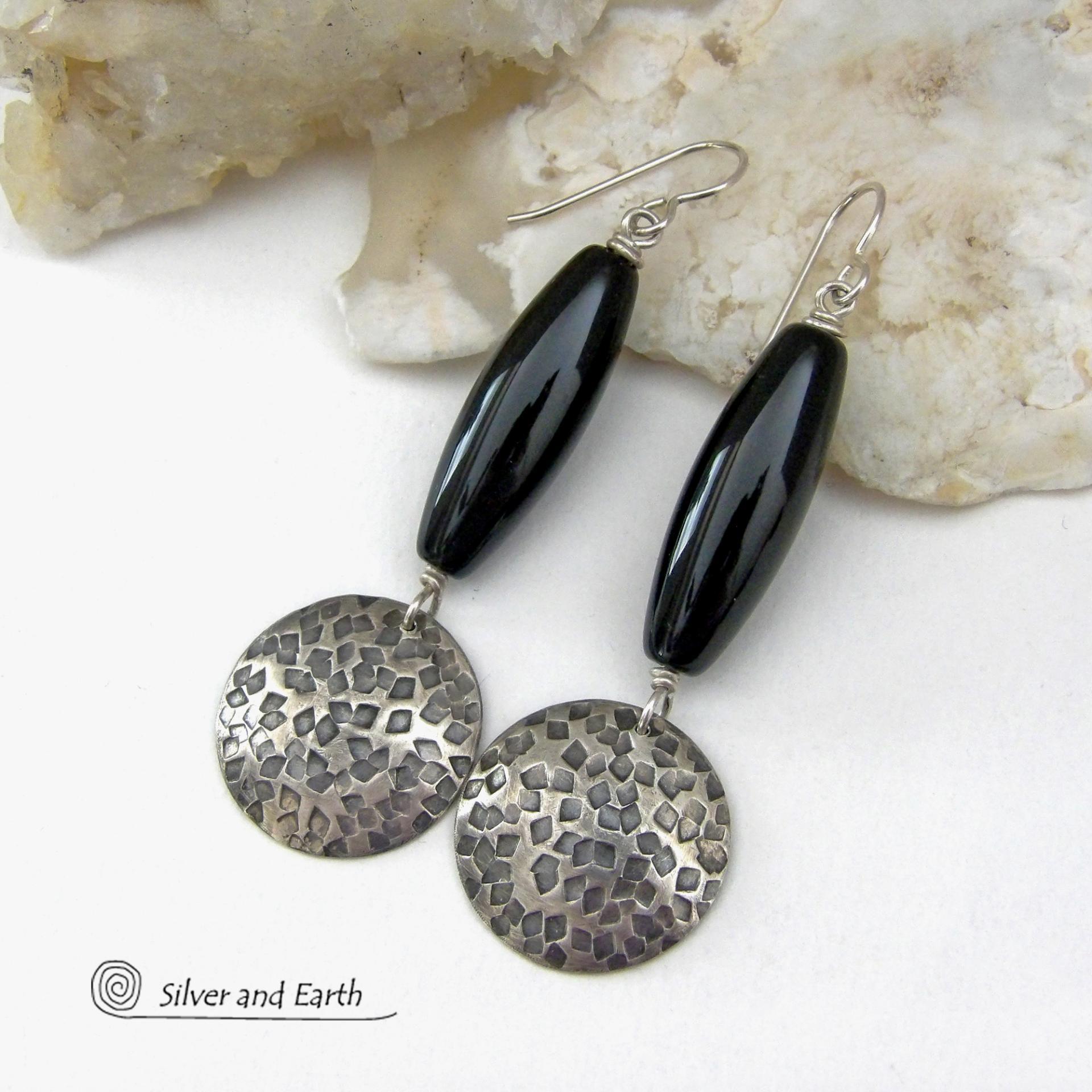 These handcrafted sterling silver dangle earrings have a hand stamped texture and oxidized finish and feature long black onyx gemstones. The stones are cut into a unique, elongated tubular shape and have a rich black hue and high polish. They have a modern, contemporary style that will look great with all wardrobe types. 