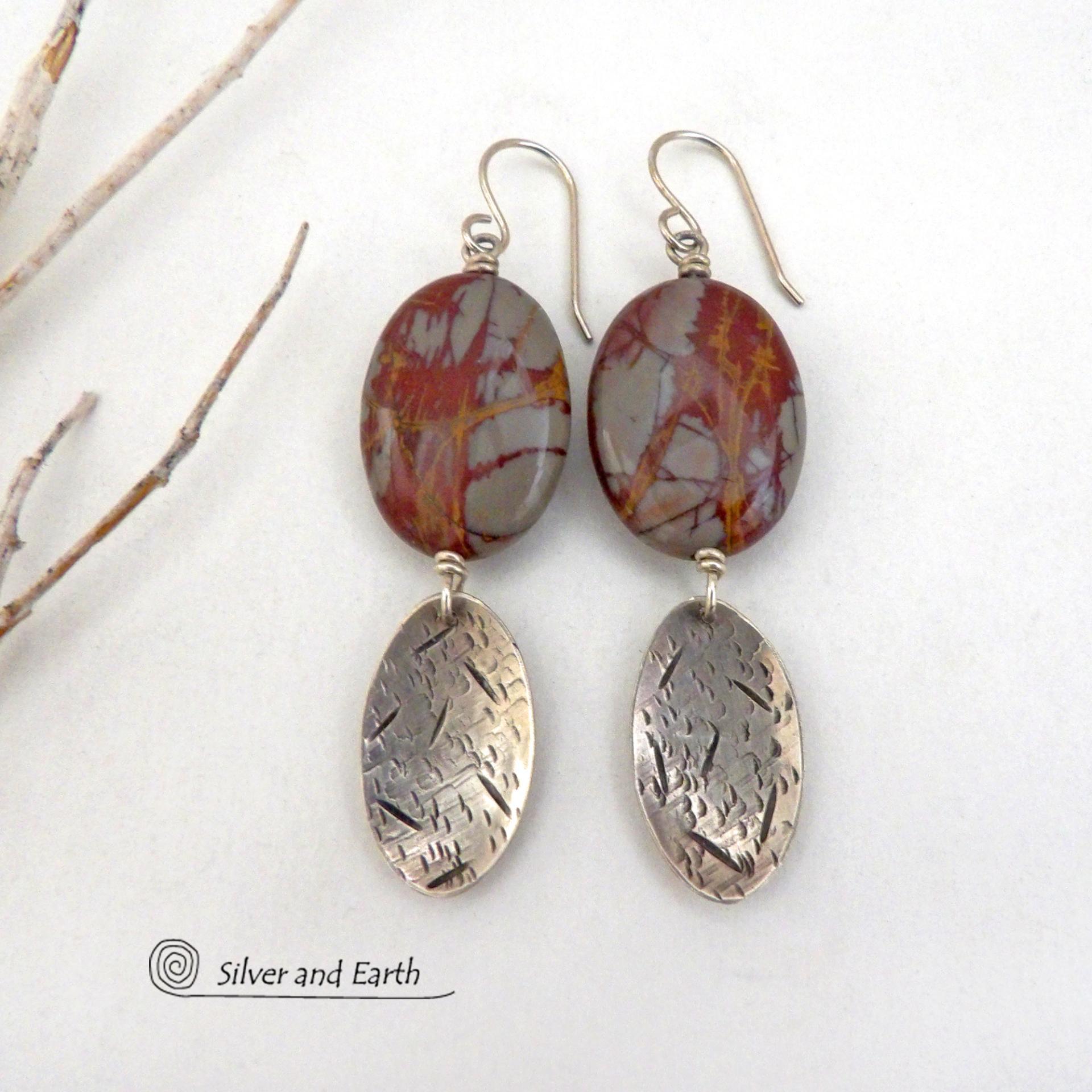 These handcrafted one-of-a-kind earrings feature natural Noreena jasper gemstones accented with textured sterling silver dangles. This stone is known for its dramatic abstract and geometric patterns and is found only in the Pilbara region of Western Australia. The stones in this pair have a great pattern consisting of hues of deep burgundy-red with fiery orange and gray streaks. They'll make a great gift for women that appreciate and love unique natural stones. Handmade by Silver and Earth.