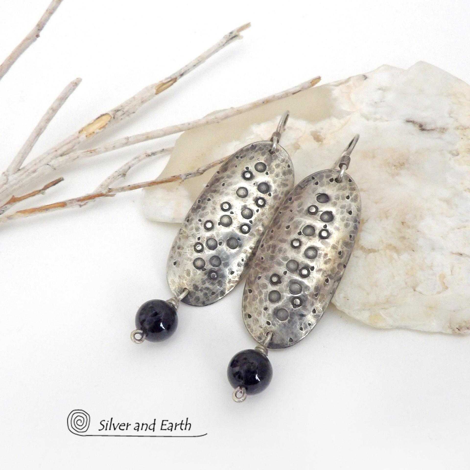 These handcrafted sterling silver earrings have a long oval shape with a hammered and hand stamped texture. Black onyx gemstones dangle from the bottom. They have a modern, earthy organic vibe that coordinates well with all wardrobe styles. Earrings are handmade in the USA by Silver and Earth Jewelry. 